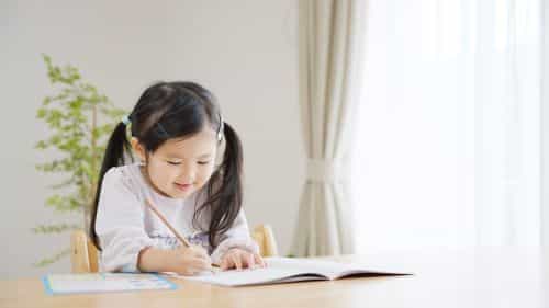小学生の女の子が机の上で鉛筆を持ち、笑顔で勉強している写真