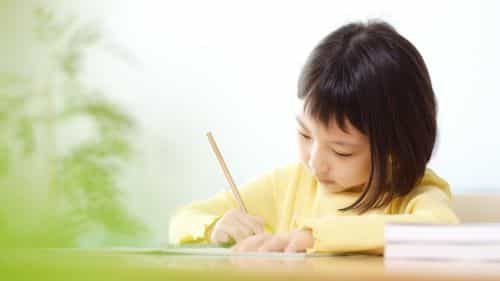 小学生が机の上で鉛筆を持ち、真剣に勉強している写真